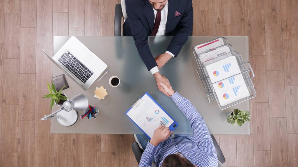Two people agreeing terms across a desk before documents are signed