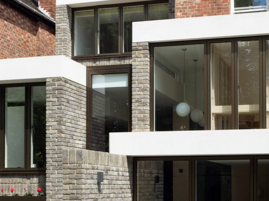 Contemporary co-living home with a blend of red brick and exposed grey brick façade, large glass panels, compact architecture, and minimalist outdoor space.